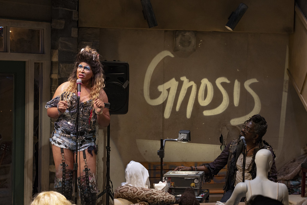Hedwig looks out while Yitzhak looks at Hedwig; the word "Gnosis" is projected behind them.