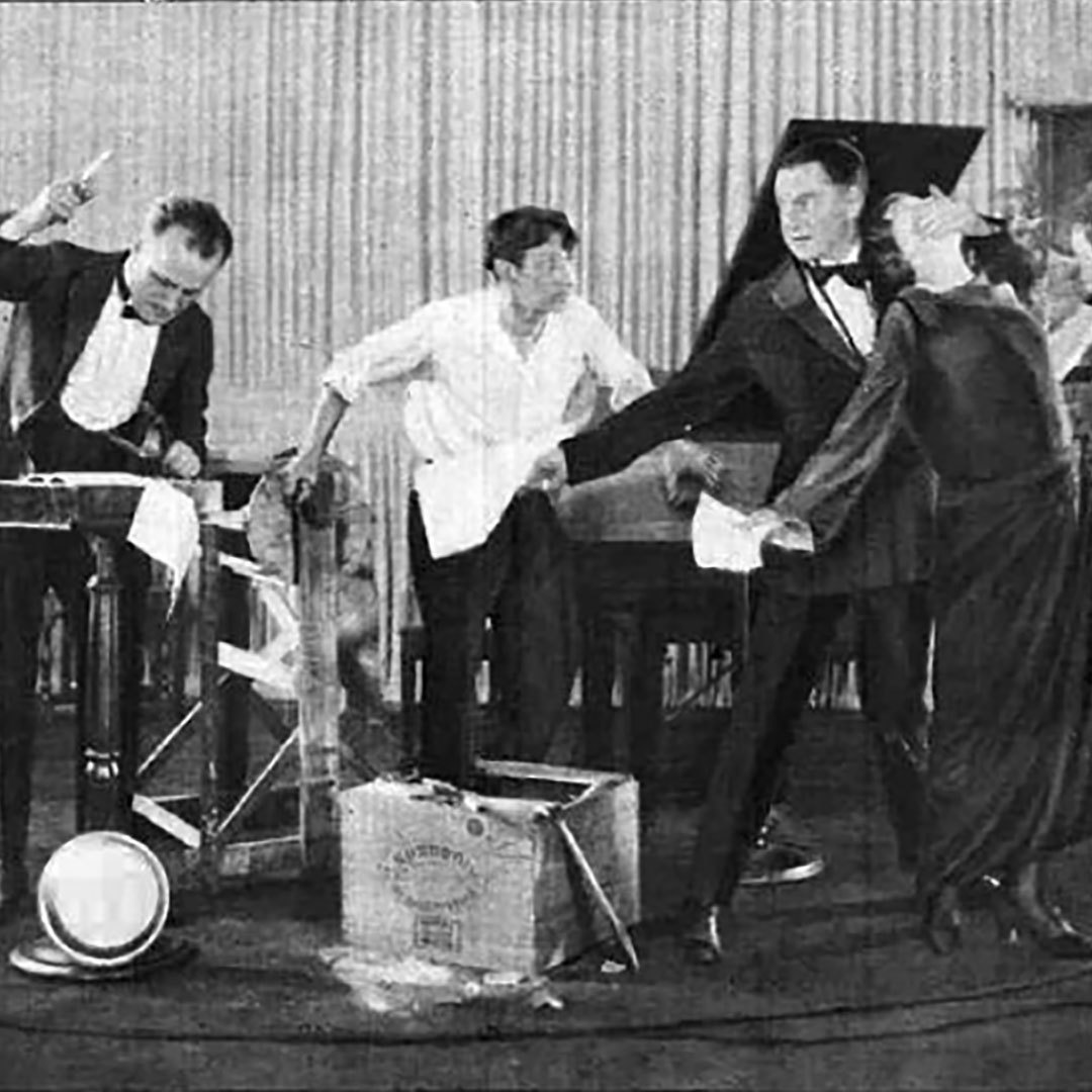 Vintage photo of four performers putting on a radio broadcast, including one man striking an object to produce sound effects.
