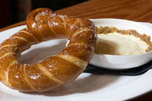 A delicious-looking soft pretzel and a small ramekin of dipping sauce arranged on a plate.