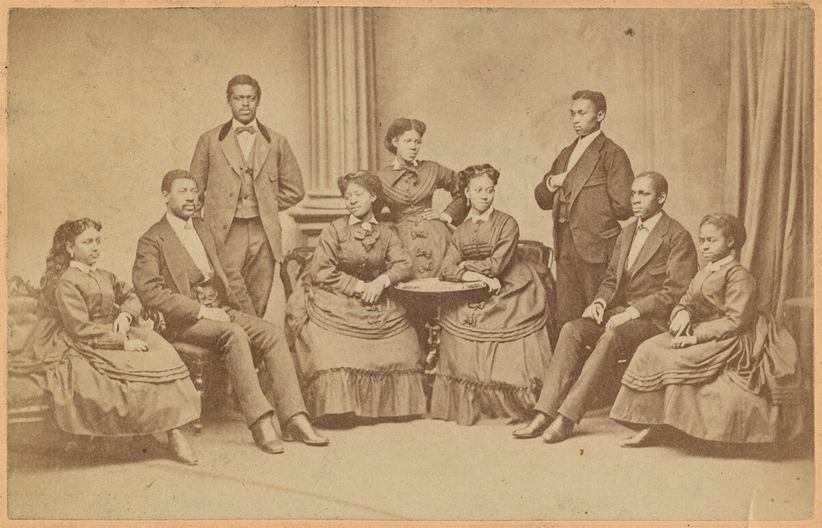 Vintage photo of a group of Black men and women seated and standing, wearing late 19th-century clothing.