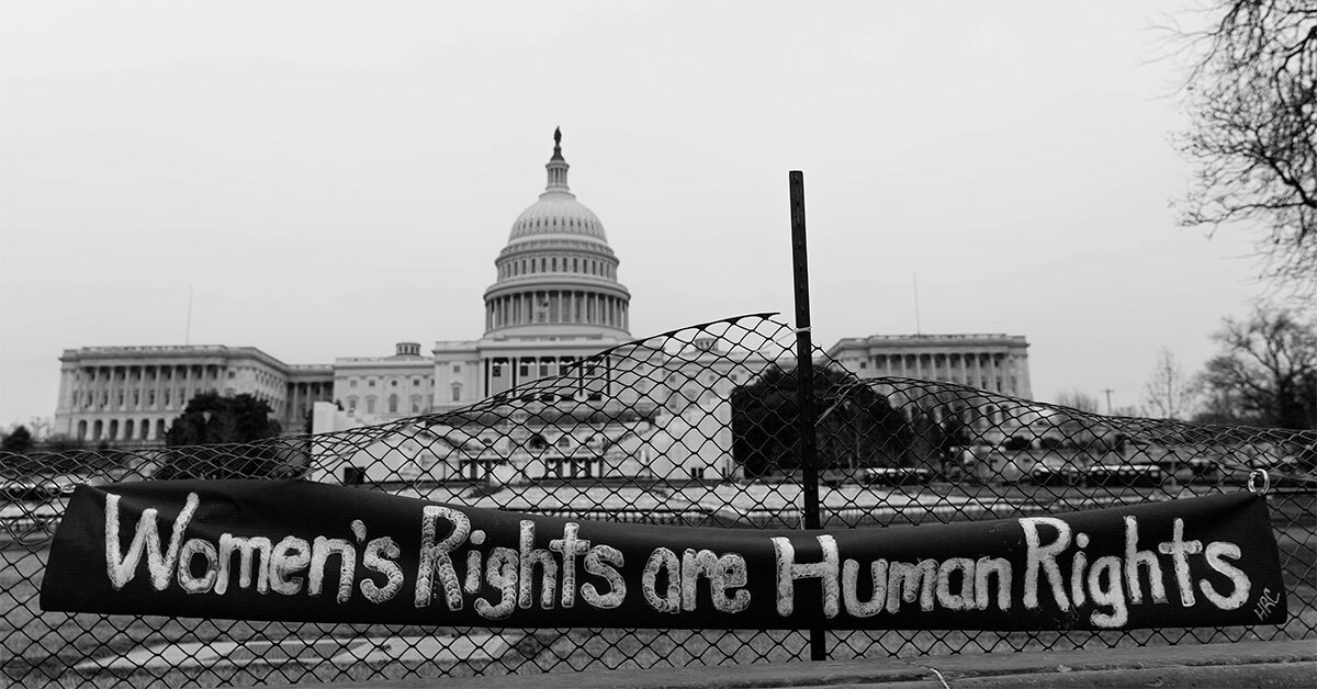 A banner that reads "Women's Rights are Human Rights" hangs on fence in front of the U.S. Capitol building.