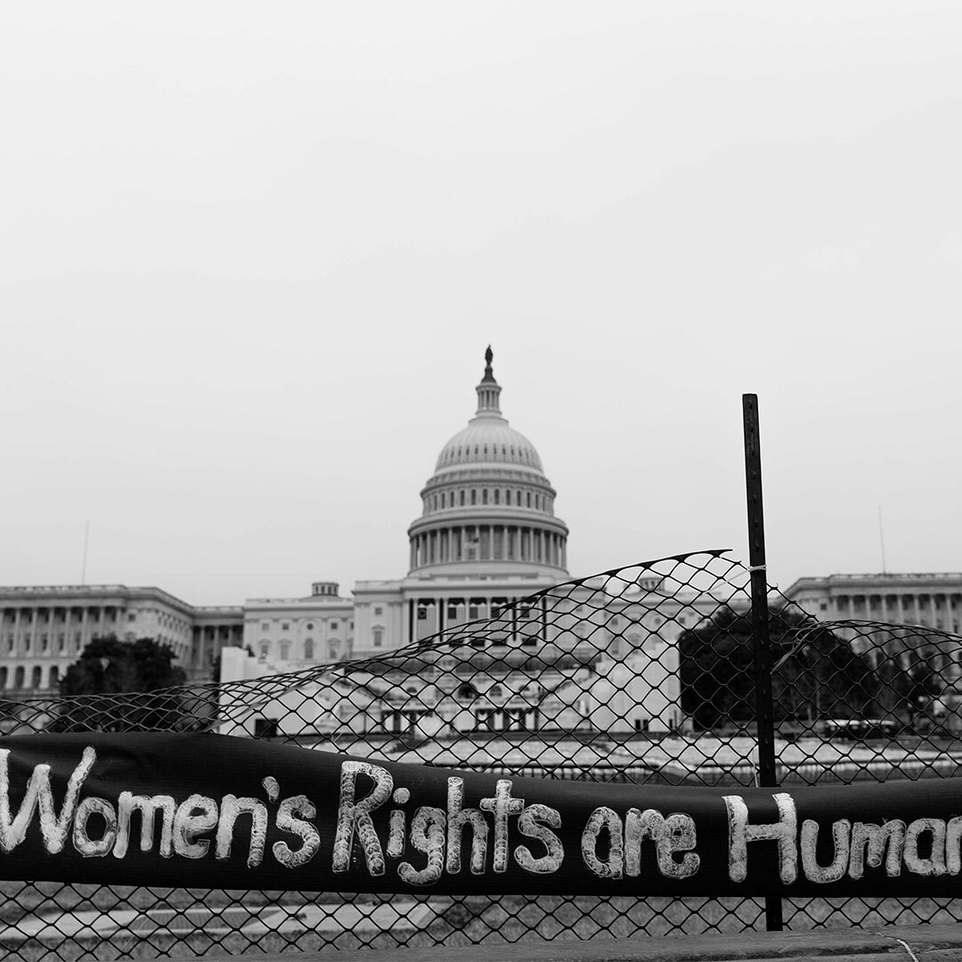 A banner that reads "Women's Rights are Human Rights" hangs on fence in front of the U.S. Capitol building.