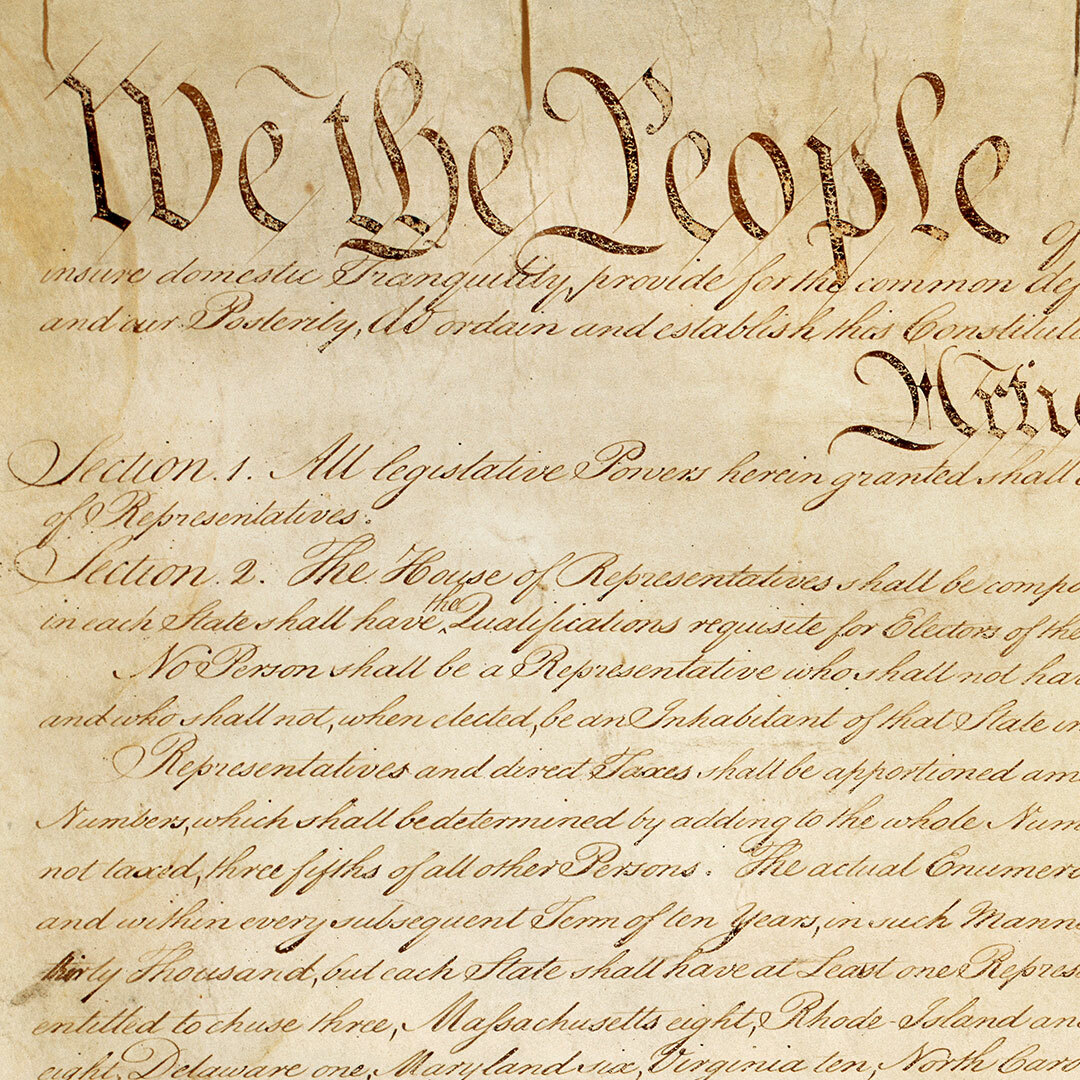 The first page of the U.S. Constitution on yellowed parchment cropped to highlight the words "We the People" and a portion of Article I.