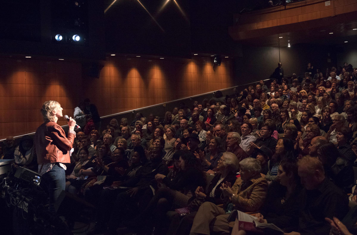 Artistic Director Marissa Wolf stands speaking in front of a large PCS audience.