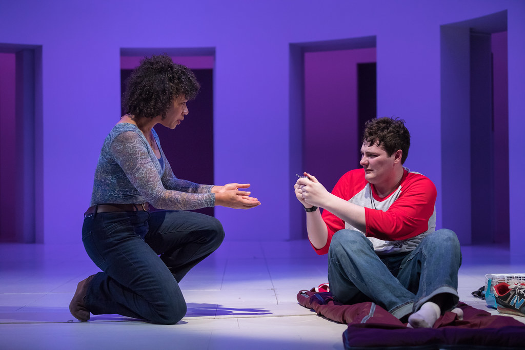 A woman gently kneels and reaches her hands out to to a young man who is brandishing a Swiss Army Knife