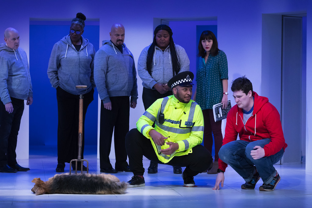 A police officer interrogates a young man; to their right is a dog, dead from being stabbed with a pitchfork