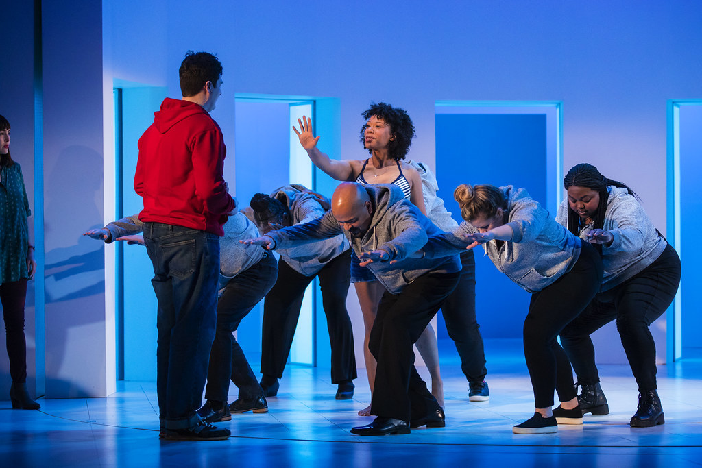 A woman is surrounded by people acting as ocean waves as she reaches out to a young man