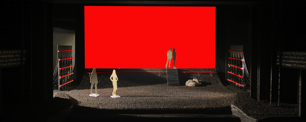 Black scale model of a stage, where cutout figures of people stand on a slope of simulated dirt in front of a bright red rectangular screen.