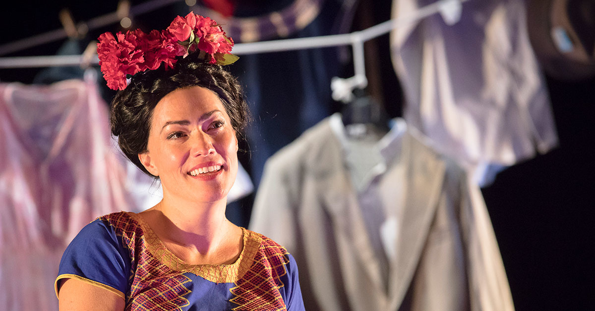 A woman dressed as Frida Kahlo with flowers in her hair smiles as though smitten.