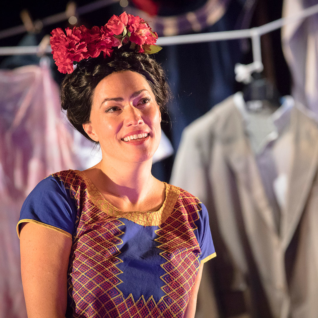 A woman dressed as Frida Kahlo with flowers in her hair smiles as though smitten.