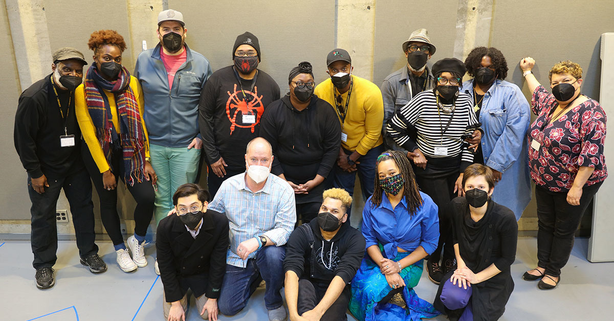 A group of 15 people gathered closely together, wearing masks.