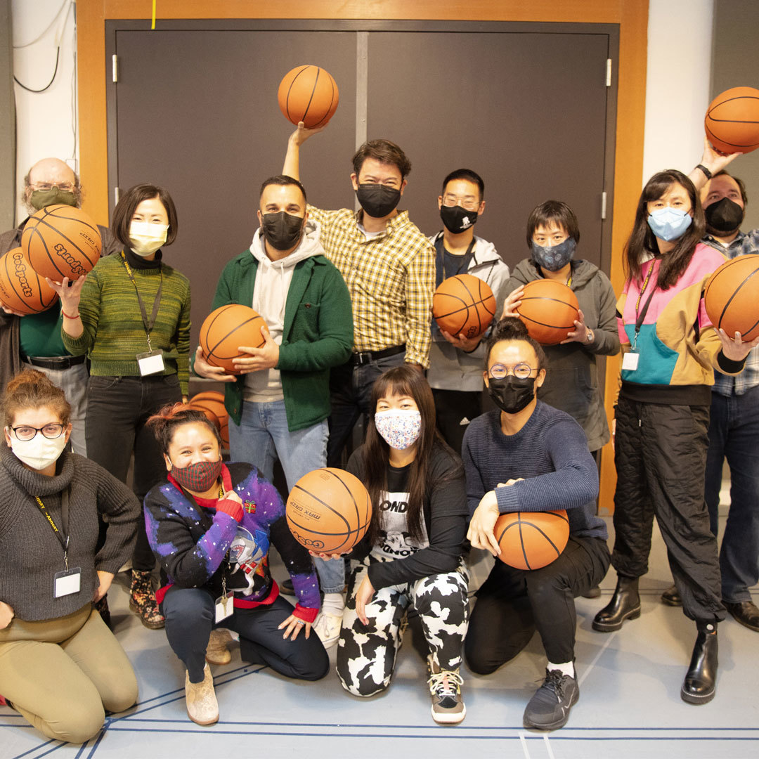 A group of masked people gather closely together smiling and holding basketballs