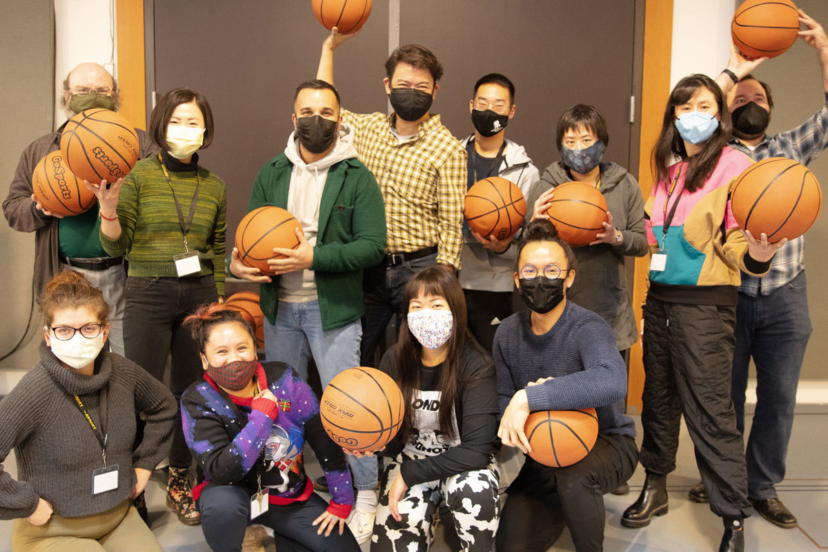 A group of masked people gather closely together smiling and holding basketballs