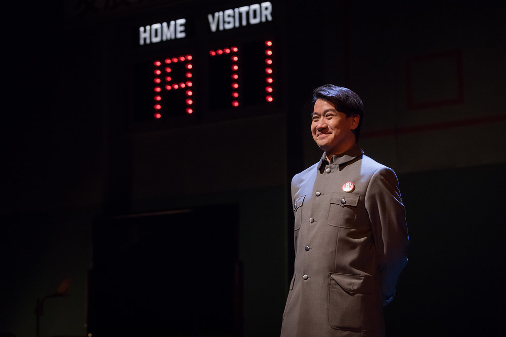 A man smiles, facing outward; a score board behind him reads "1971"