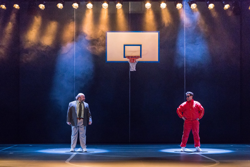 Two men stare across each other from across a basketball court; stadium lights illuminate the stage