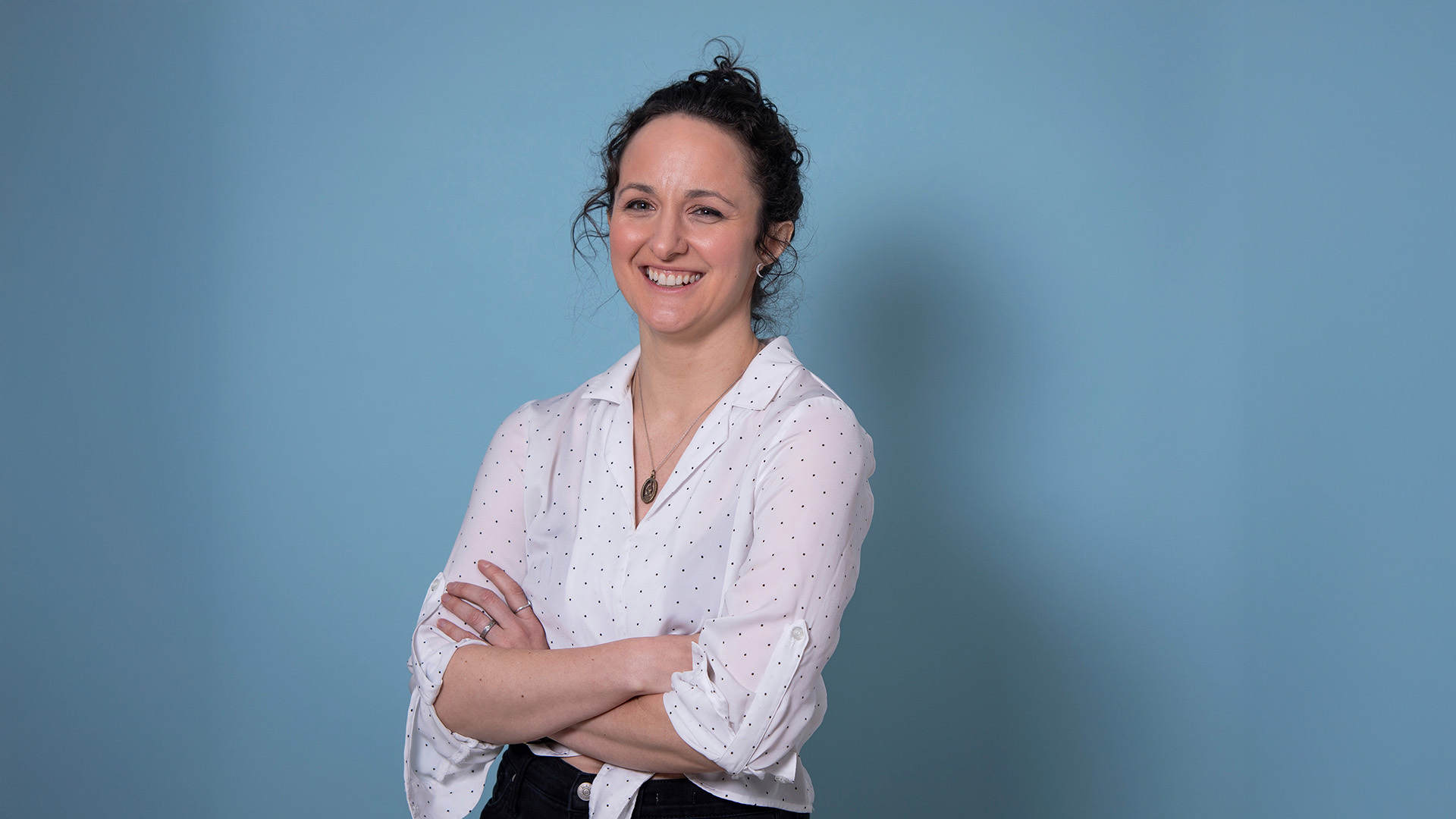white woman with brown hair in a bun standing with her arms crossed in a white button down blouse.