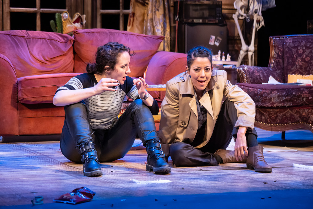 Two women sit on the floor; they are in deep deduction.