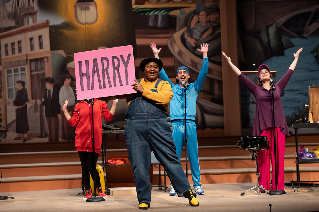 A group of people stand and cheer; a person in the foreground holds a sign that reads "HARRY".