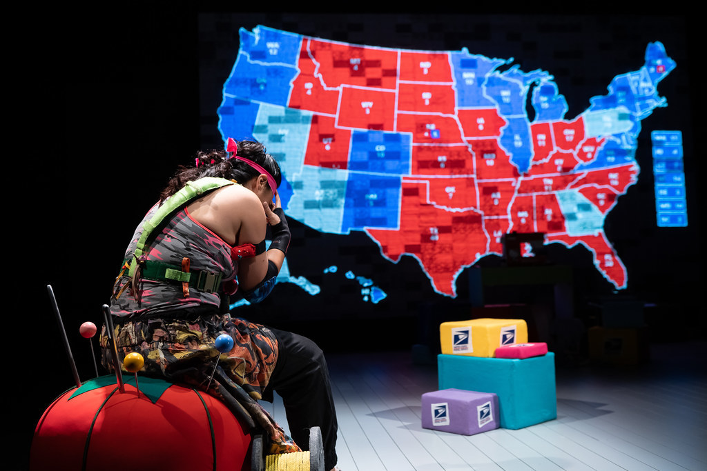 A woman holds her head in her hands; a projection of the 2020 electoral map is visible in front of her.
