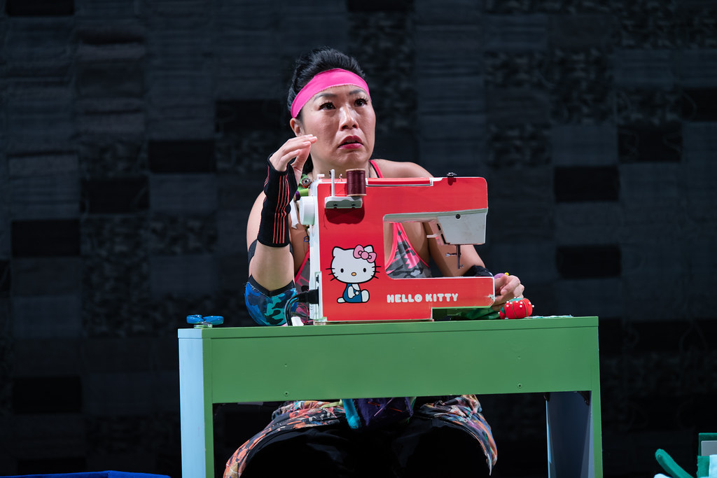 A woman sits at a table. On it sits a Hello Kitty sewing machine. She looks off at something in the distance, concerned.