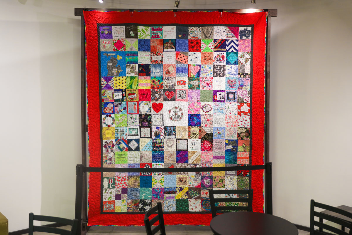 A large quilt hanging on a wall in a gallery-style display, within the Ellyn Bye Studio lobby of The Armory.
