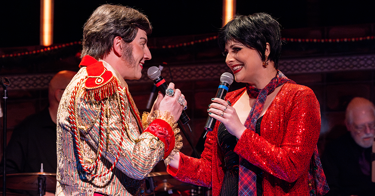 A man in a red & gold coat with epaulets and a woman in a red sequined top smile and sing to each other holding mics.