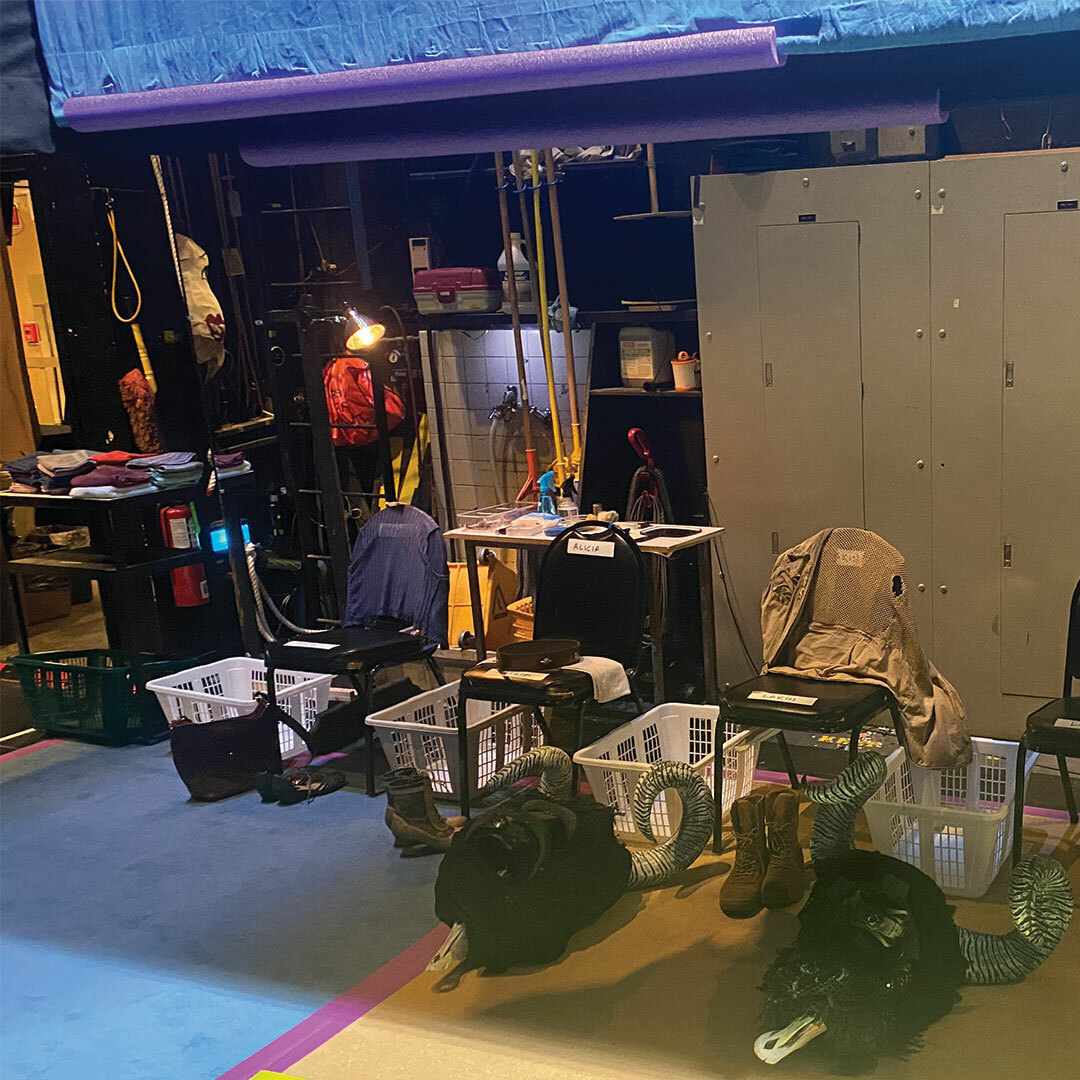 Various props, costume items, and laundry baskets gathered on the floor and stacked on chairs in a backstage area.