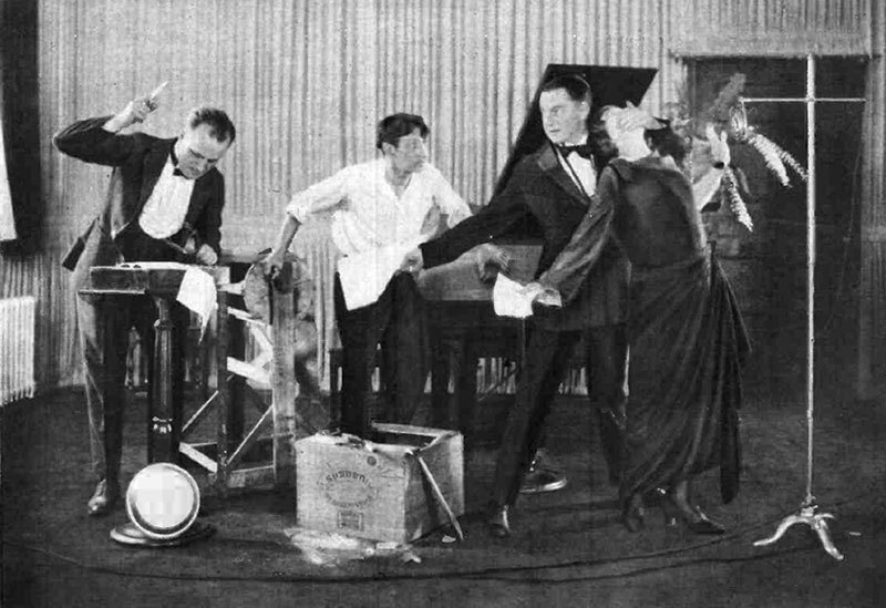 Vintage photo of four performers putting on a radio broadcast, including one man striking an object to produce sound effects.