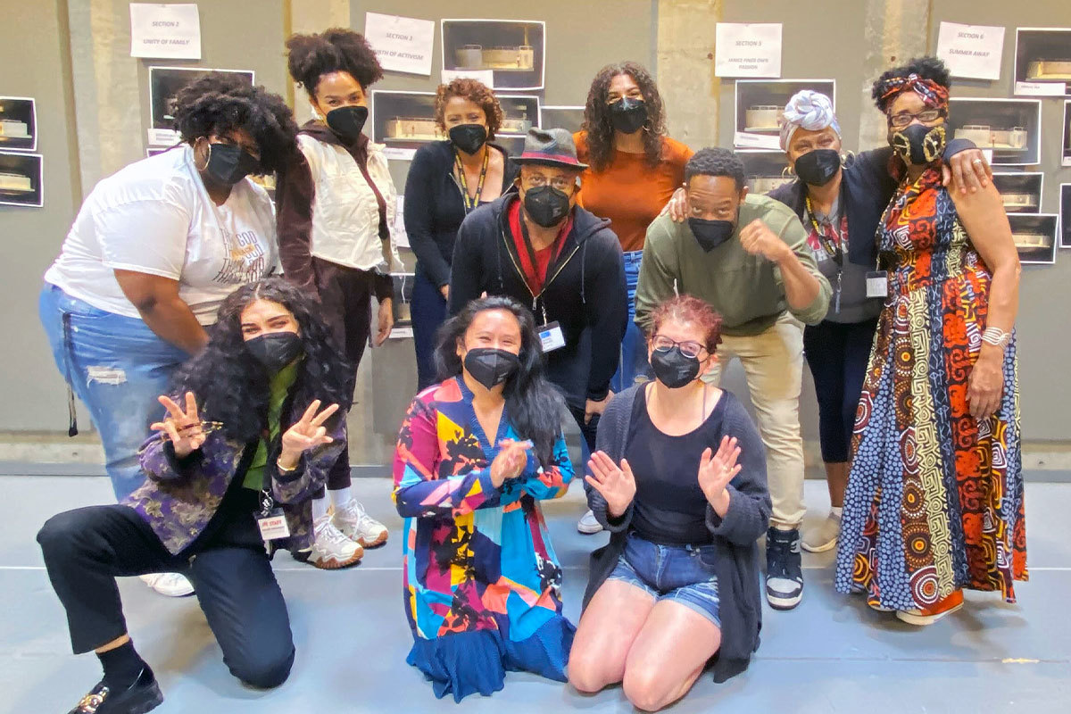A group of people stand near each other, masked, and smile/pose for a picture.