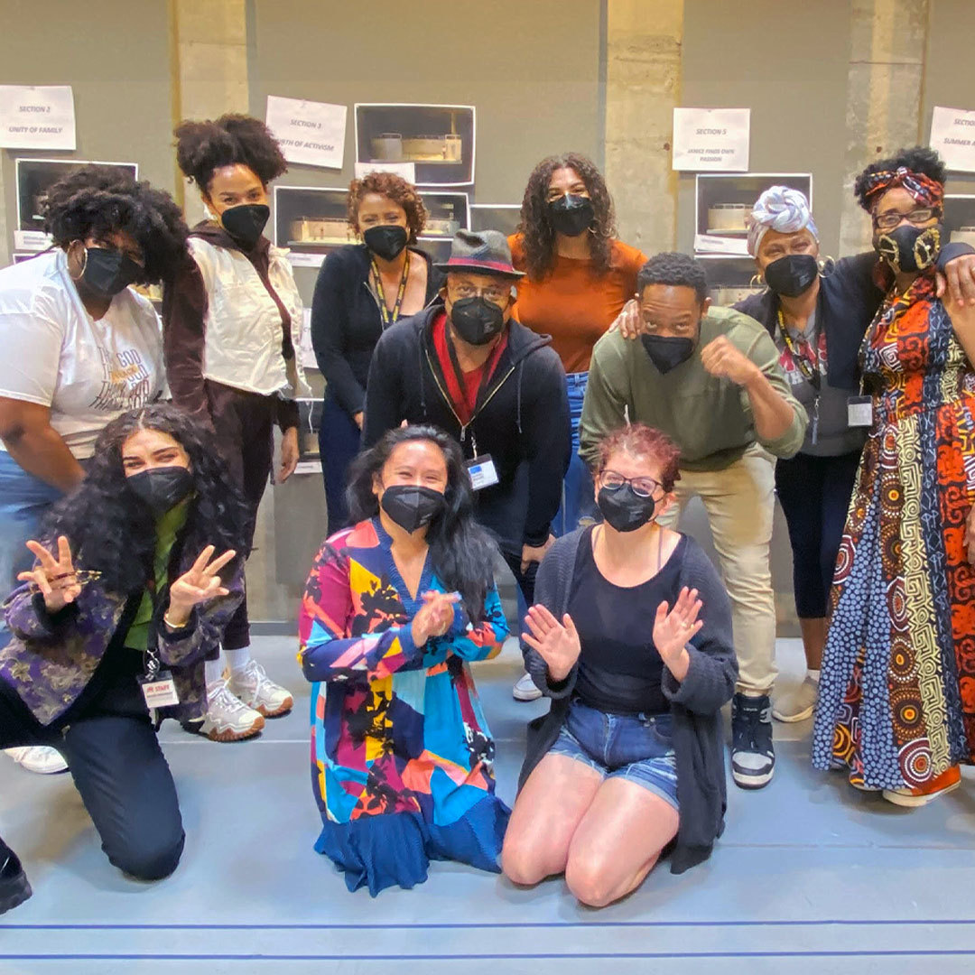 A group of people stand near each other, masked, and smile/pose for a picture.