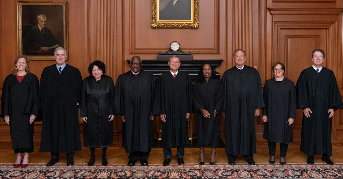 Nine smiling men and women wearing black robes stand posing side-by-side in a wood-paneled room.