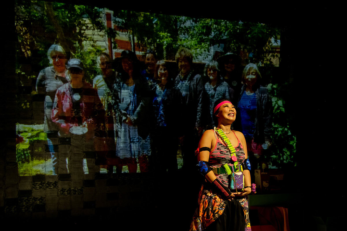 A woman stands and smiles in front of a projection; the image is of a group of women, smiling.