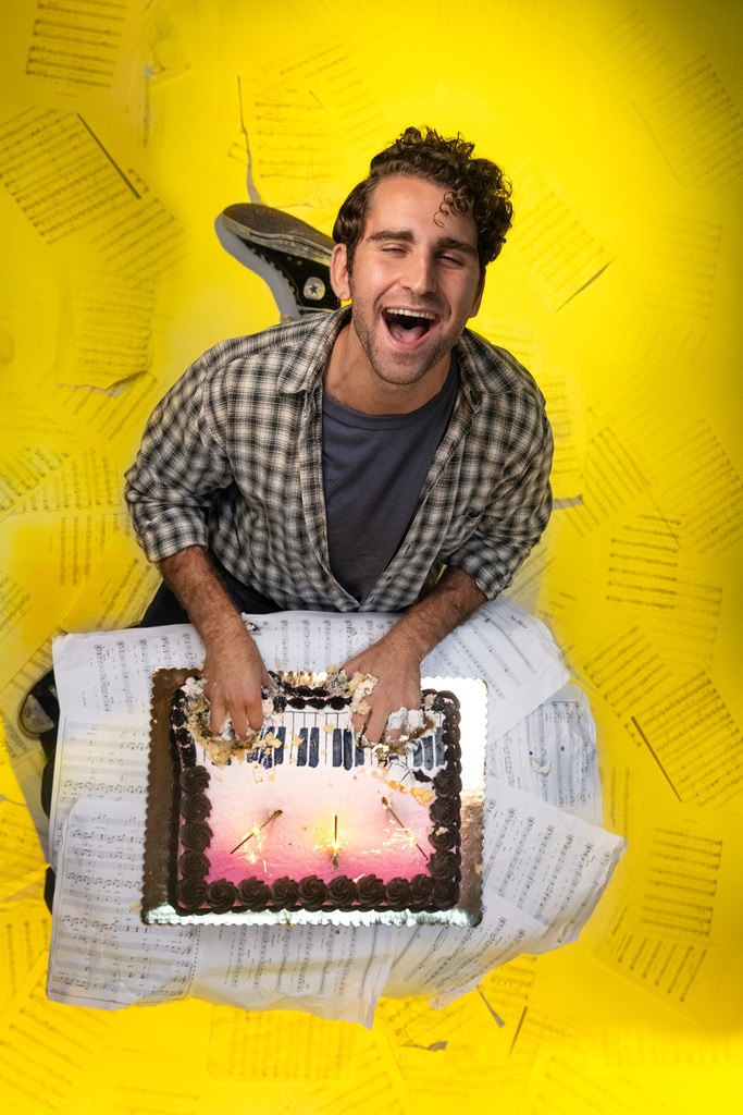A man kneels in front of a cake playing it like a piano; he is in a state of elation.