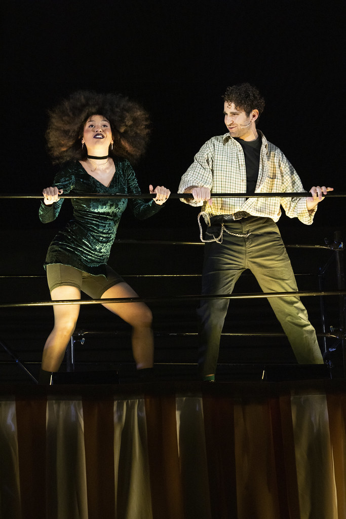 A man and a woman in cool 90s clothing dance while holding on to a railing.