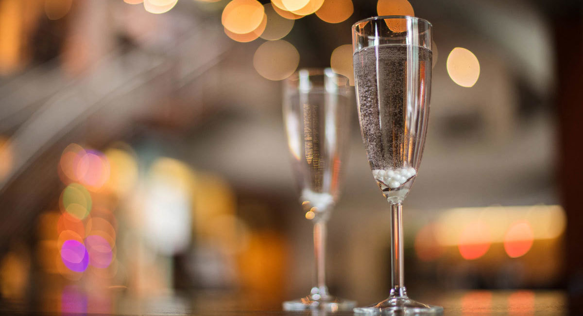 Close-up view of two filed champagne flutes with The Armory's lobby in the background.