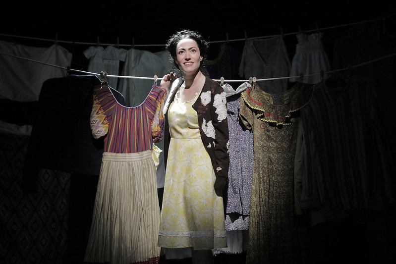 Vanessa Severo as Frida, standing in front of a clothesline, with an outfit hanging on either side of her.