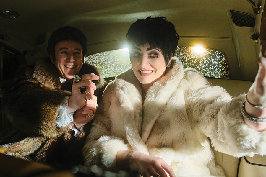 A flamboyantly dressed man and woman smiling in the backseat of a car.