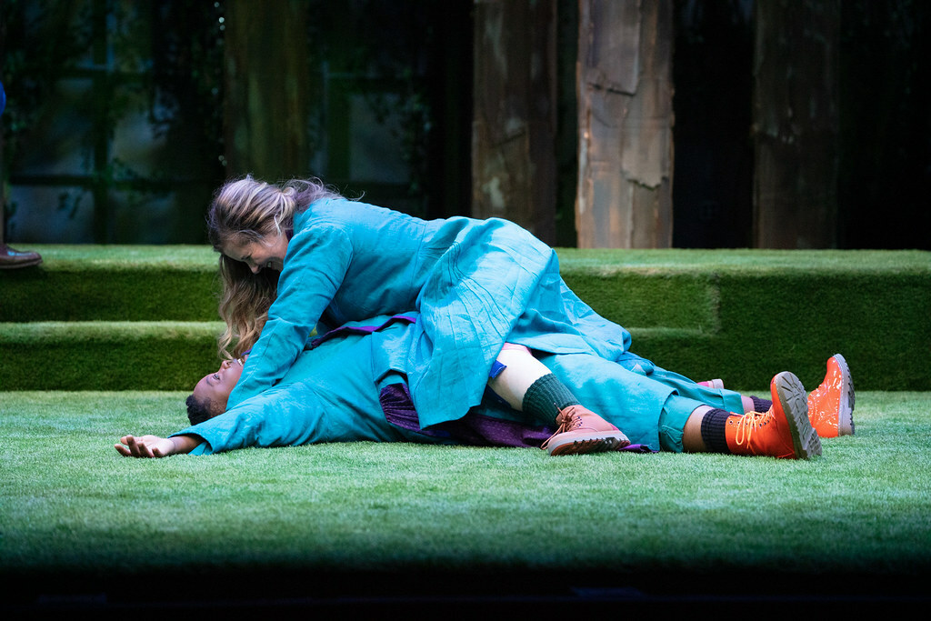 A person is lying on top of another person, apparently pinning them down on the stage floor which is covered in green turf.