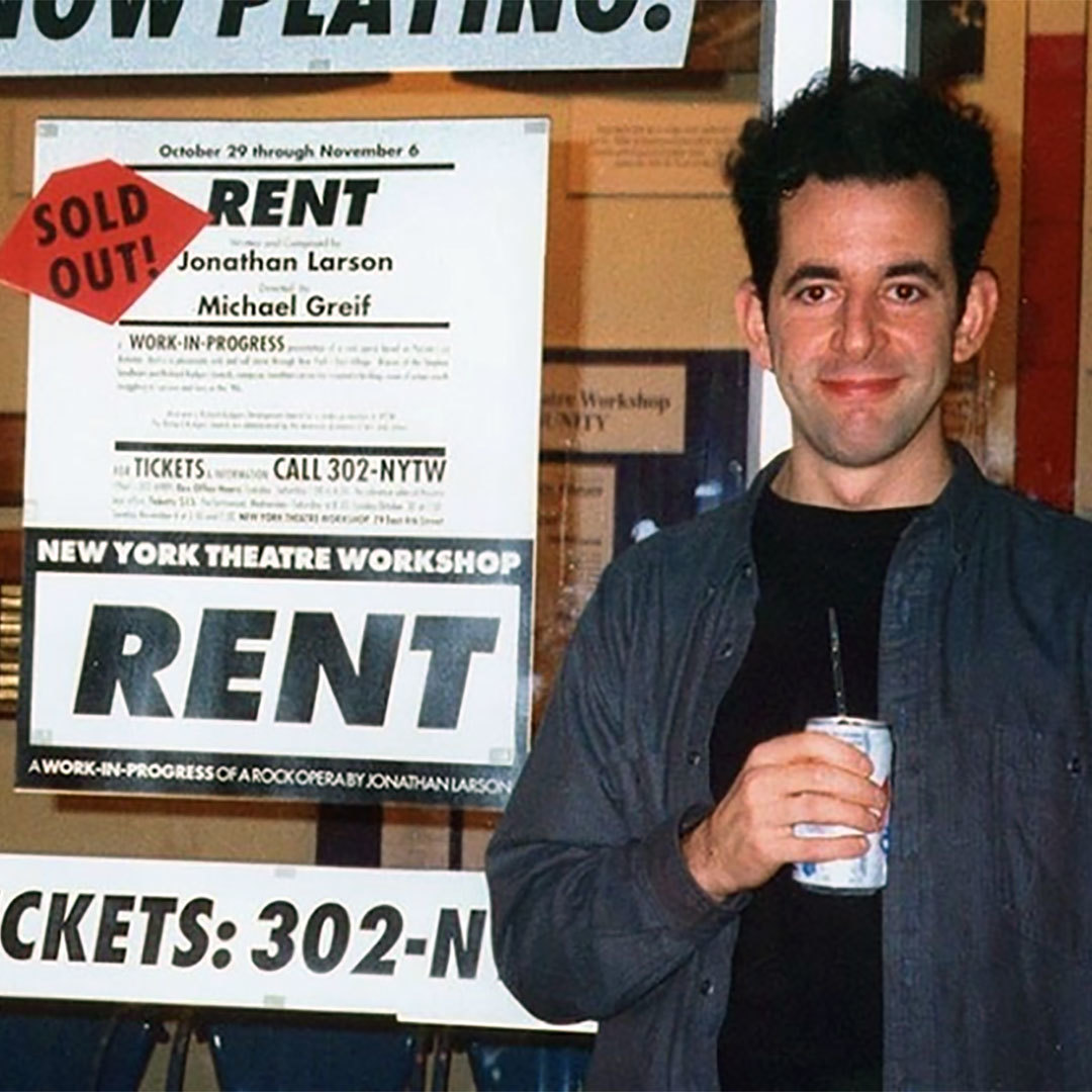 A man stands to the right of a poster advertising tickets to Rent at NY Theatre Workshop with a notice in red that says "Sold Out."