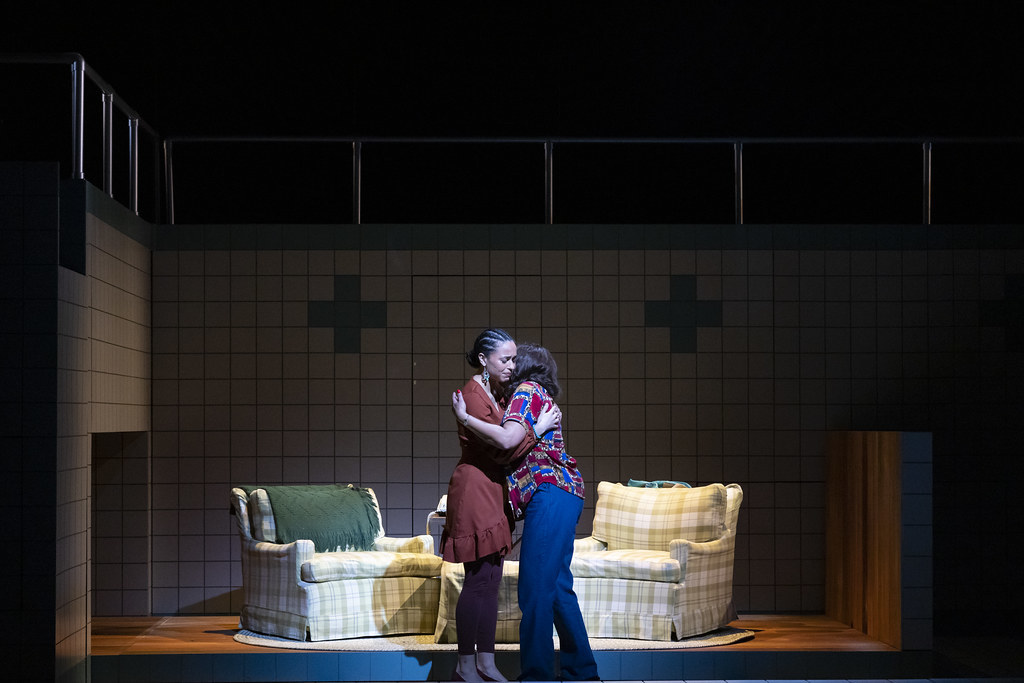 Two women share a hug center stage in a dramatic lighting; it is tender and emotional.