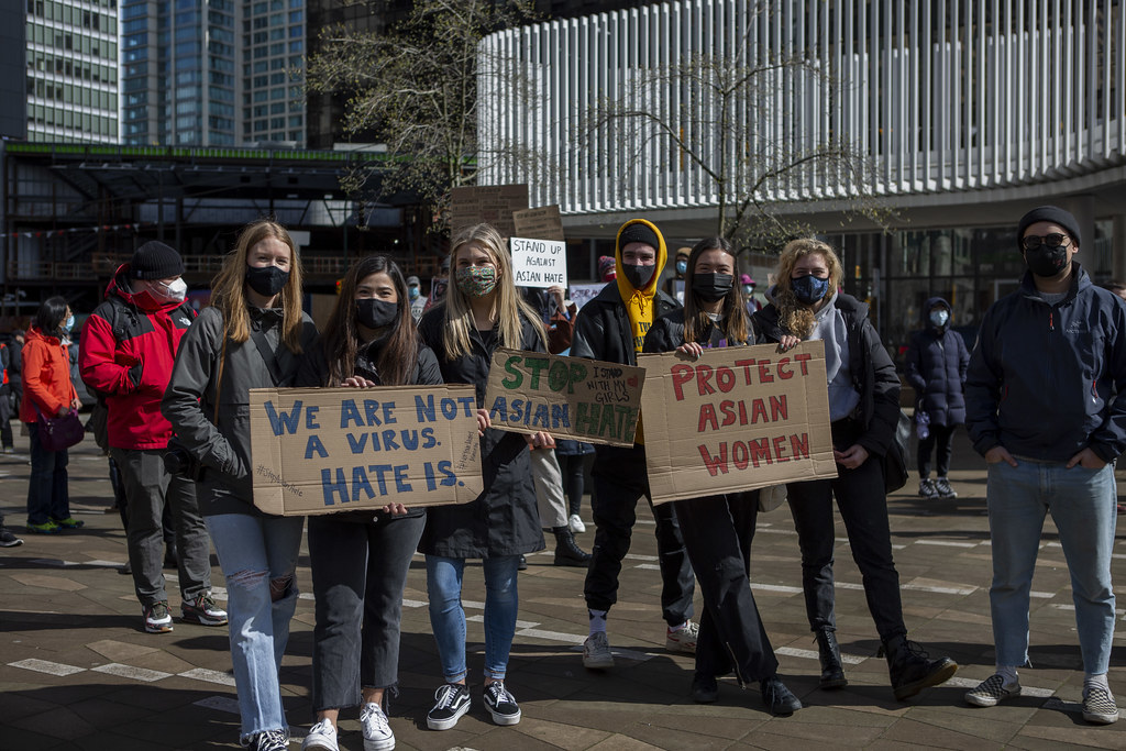 A group of protesters on a city street hold signs saying "We are not a virus. Hate is," "Stop Asian hate," and "Protect Asian women."