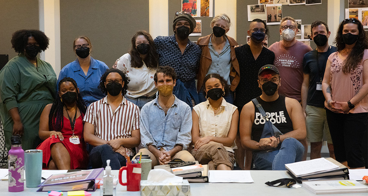 A group of 14 people gathered closely together, wearing masks.